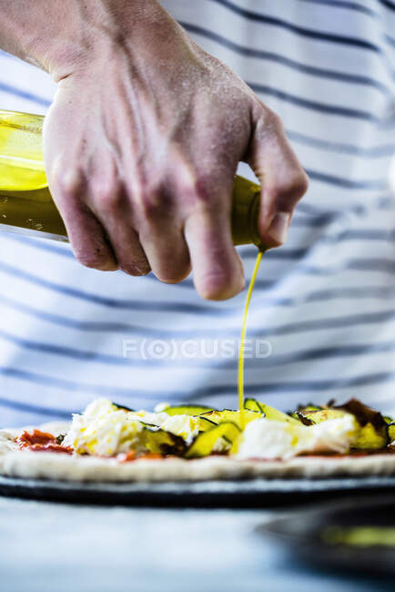 Poring olive oil on pizza with courgette, mozzarella cheese, and tomato sauce — Stock Photo