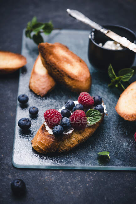 Toasted baguette slices with almond cream cheese, berries and mint — Stock Photo