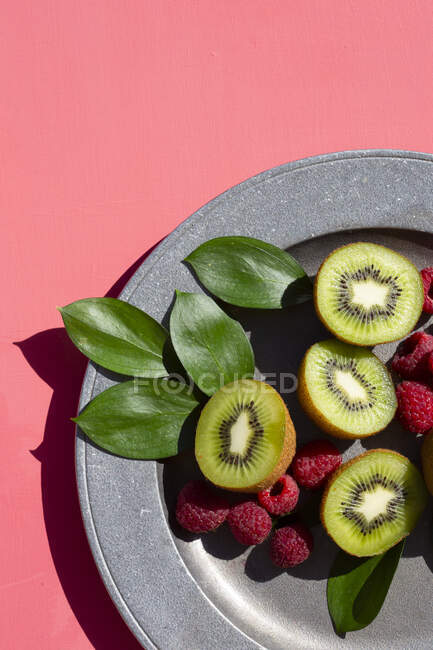 Kiwi moitiés avec des framboises sur une assiette sur une surface rose — Photo de stock