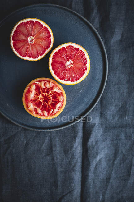 Grapefruithälften und eine Schale auf schwarzem Keramikteller vor Stoffhintergrund — Stockfoto