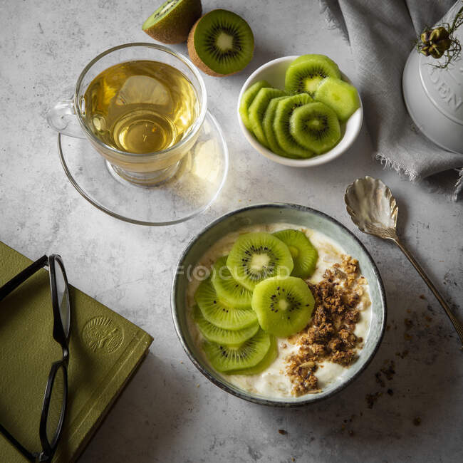 Yogurt de fruta kiwi con granola en el desayuno con té en taza de vidrio - foto de stock