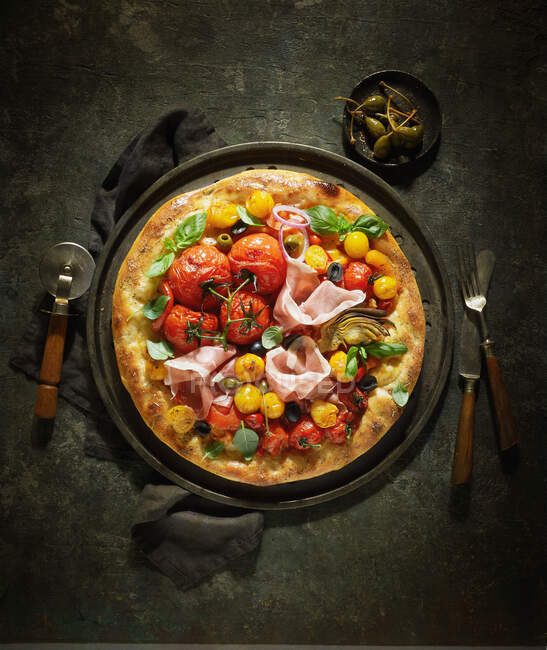 A pizza topped with tomatoes, ham and caper apples — Stock Photo