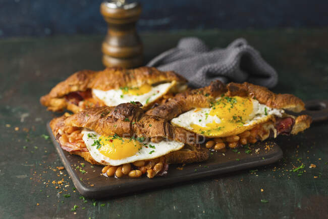 Круассаны, запеченные с сыром, бобами и жареными яйцами, посыпанные петрушкой — стоковое фото