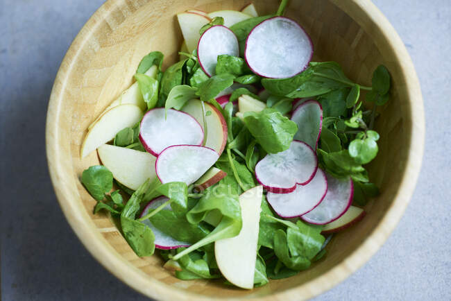 Lambs lettuce with apple and radish slices in a wooden bowl — Stock Photo