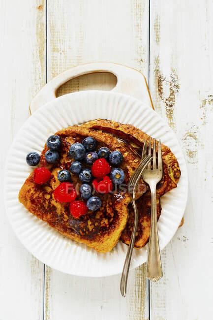 Французькі тости з ягодами і кленовим сиропом на тарілці з виделками. — стокове фото