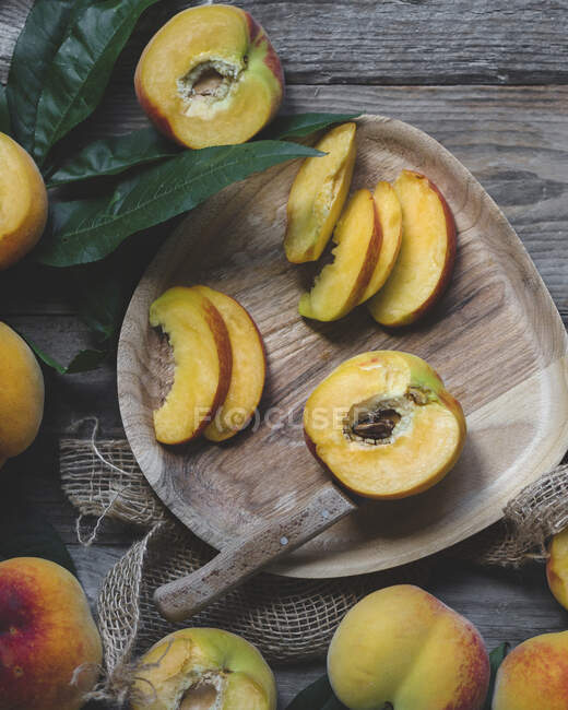 Wooden plate of cut peaches with leaves and knife — Stock Photo