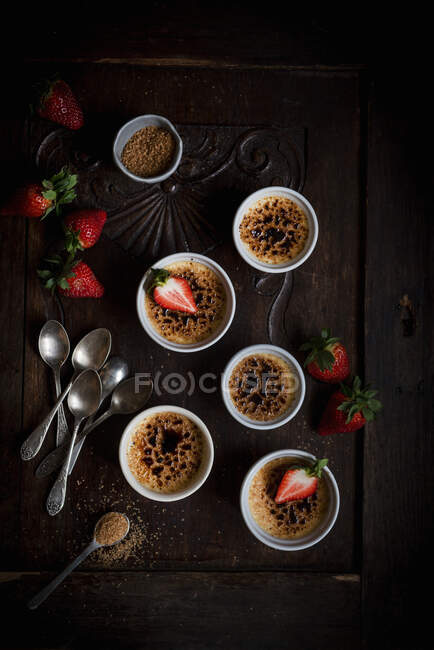 Porciones de Creme Brulee en cuencos con fresas frescas y cucharas - foto de stock