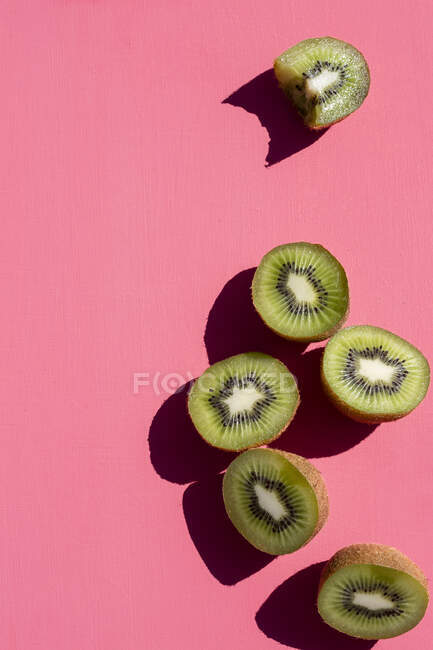 Mitades kiwi, una con una mordedura sacada, sobre una superficie rosa - foto de stock