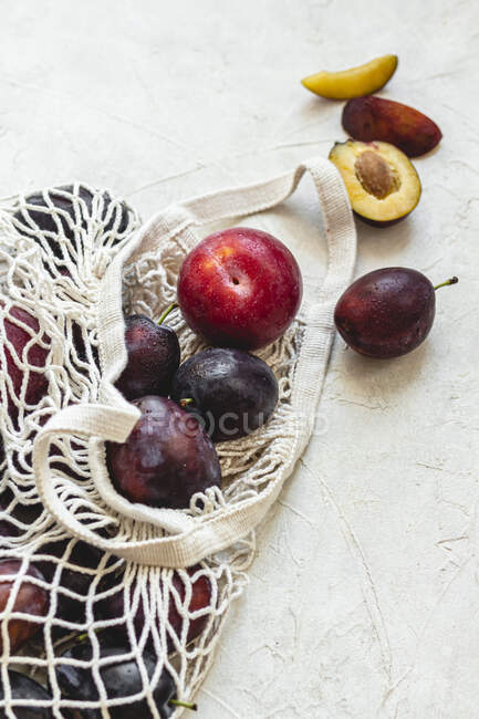 Plums in crochet bag and on concrete surface — Stock Photo