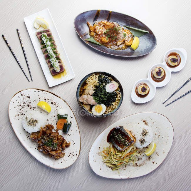 Moderne japanische Gerichte auf einem Tisch: Chicken Ramen, Thunfisch Tataki, Soba Chicken, Ebi Chilli Sauce, Gegrillter Lachs und Jakobsmuscheln mit Misosauce — Stockfoto