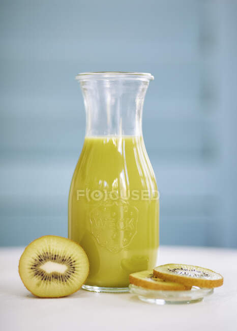 A kiwi smoothies in a glass bottle against a blue background — Stock Photo