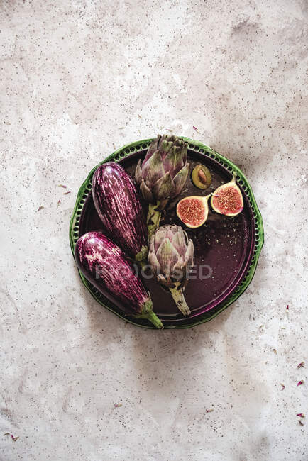 Eggplants, artichokes, figs and plums on plate, top view — Stock Photo