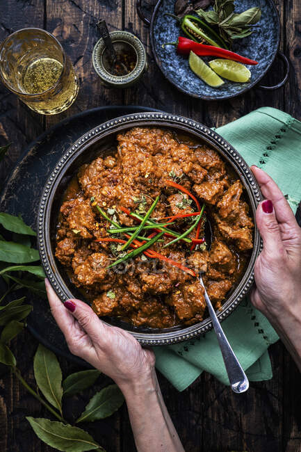 Hands holding Large bowl of lamb curry on rustic wooden table — Stock Photo