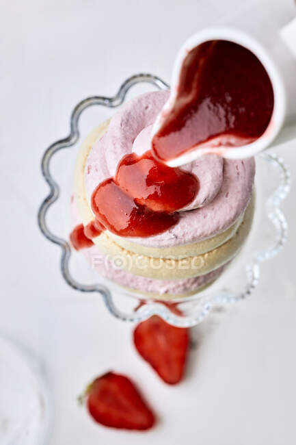 Strawberry sauce dripping from jug on pavlova dessert — Stock Photo