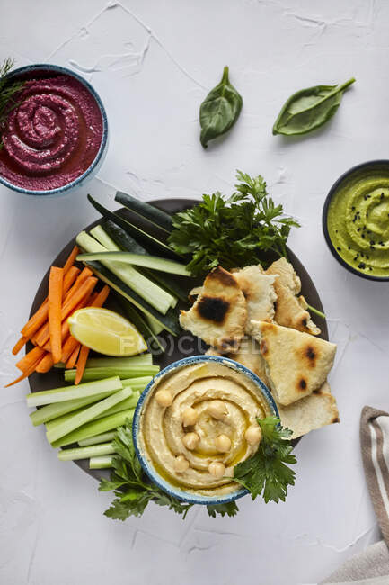 Various types of hummus served with fresh vegetables and pita bread — Stock Photo