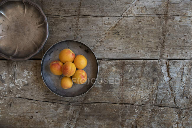 Damascos em tigela de prata e tigela de prata vazia na superfície de madeira rústica — Fotografia de Stock