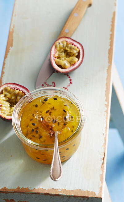 Jar of mango and passionfruit jam with halved fruit and knife on wooden chair — Stock Photo