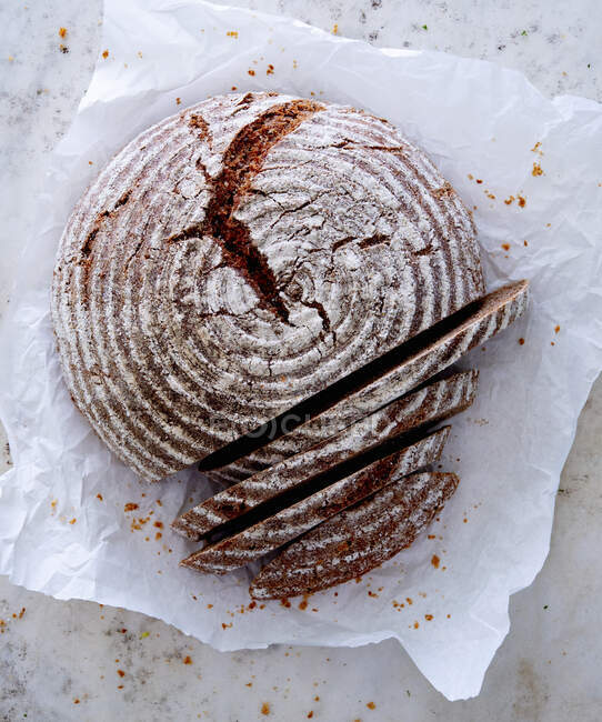 Round spelt wholegrain bread on paper, sliced — Stock Photo
