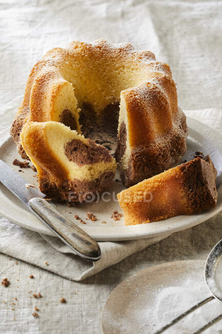 Marble cake with icing sugar, partly sliced — Stock Photo