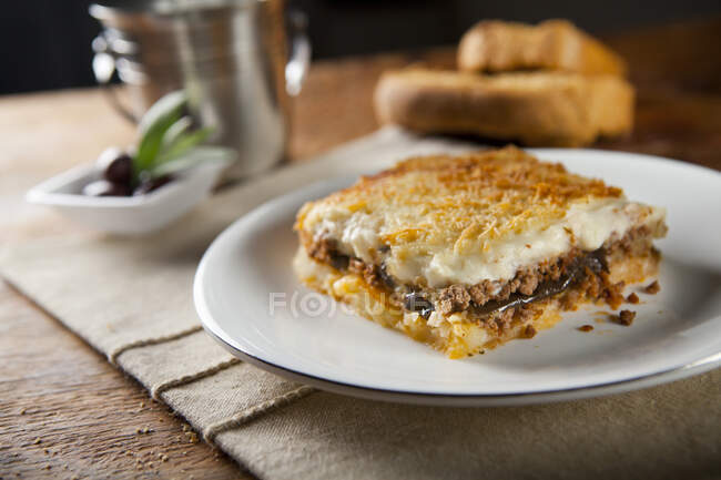 Stück griechischer Mousaka serviert auf einem Teller und Brot auf dem Hintergrund — Stockfoto