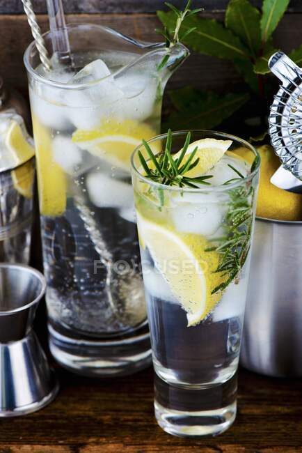 Gin und Tonic mit Zitrone, Eiswürfeln und Rosmarin zwischen Barutensilien — Stockfoto