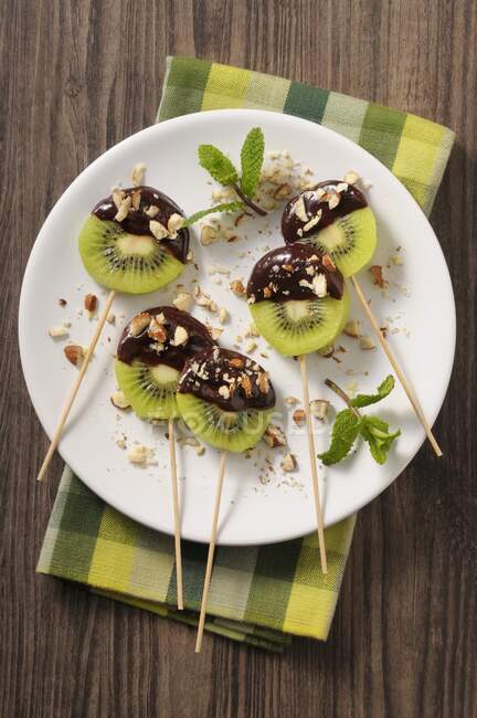 Chocolate and kiwi lollies with chopped nuts — Stock Photo