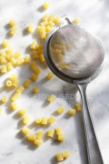 Uncooked ditalini rigate and a small strainer — Stock Photo