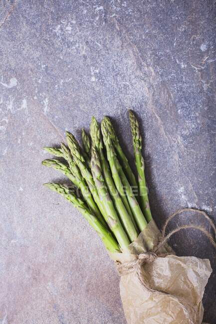 A bunch of fresh asparagus spears in a paper bag tied with string — Stock Photo
