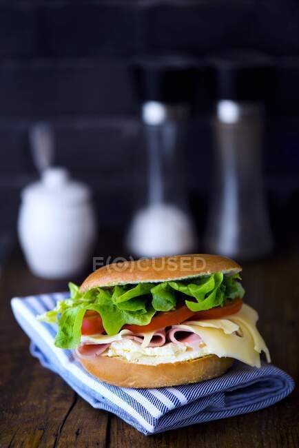 Un bagel con crema di formaggio, prosciutto cotto, formaggio, pomodoro e insalata — Foto stock