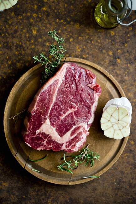 Ein rohes Steak mit Knoblauch und Rosmarin auf einem Holzbrett — Stockfoto