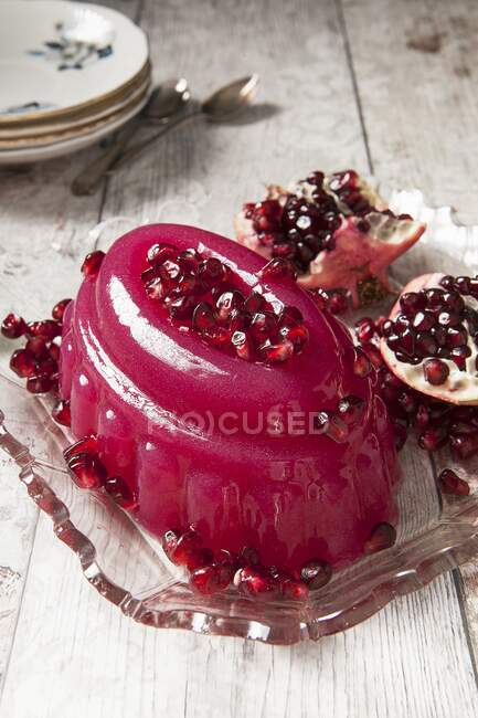 Блискучий рожевий желе, покритий насінням помгранте на старовинній скляній тарілці з розділеним помгранте на задньому плані — стокове фото