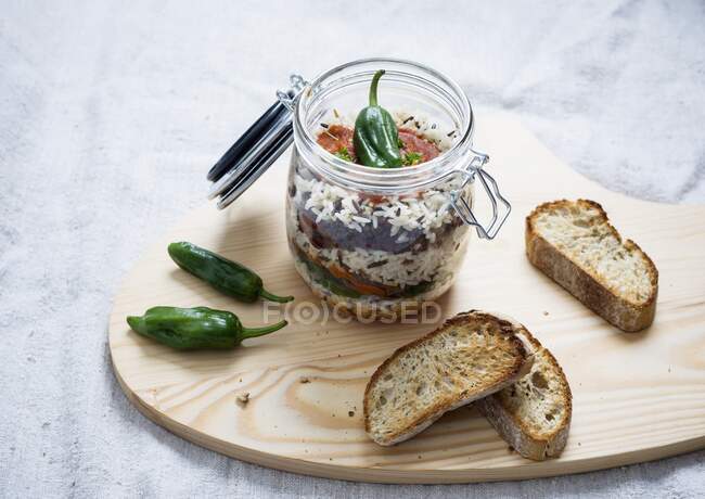 Arroz, molho de tomate, pimentas fritas, carne de soja, feijão e lentilhas em um frasco de vidro, servido com pão torrado — Fotografia de Stock