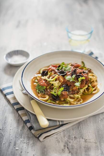 Bowl of courgetti with sauce made with tomatoes, olives, capers and anchovies — Stock Photo