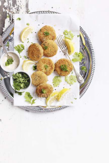 Hamburguesas de pescado con cuñas de limón y perejil en una mesa blanca - foto de stock
