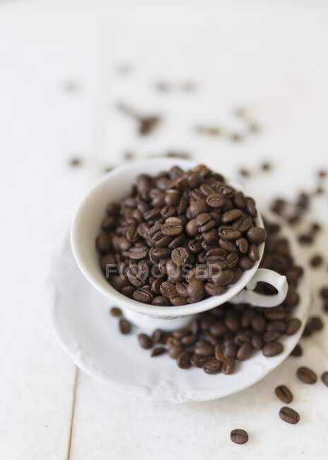 Granos de café en una taza de café y en un platillo - foto de stock