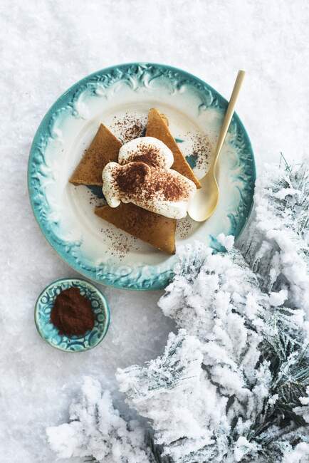 Pastel de jengibre festivo con crema batida en un plato en la nieve - foto de stock