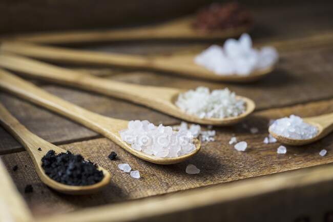 Different types of food coarse Salt in wooden spoons on dark background — Stock Photo