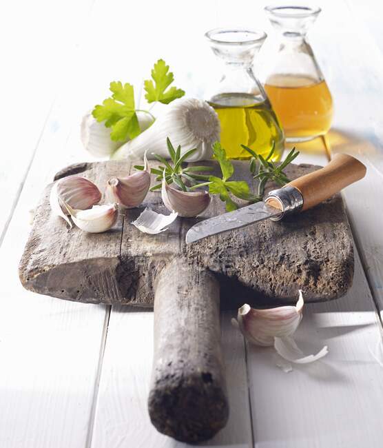 Spicchi d'aglio con olio, aceto e coltello su una vecchia tavola di legno — Foto stock