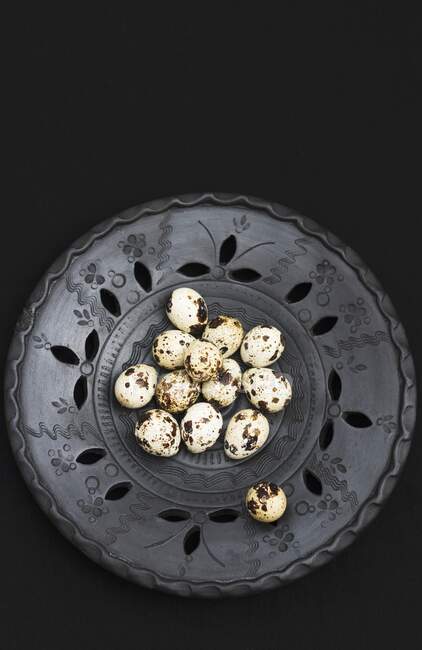 Quail eggs in black ceramic bowl on black background — Stock Photo