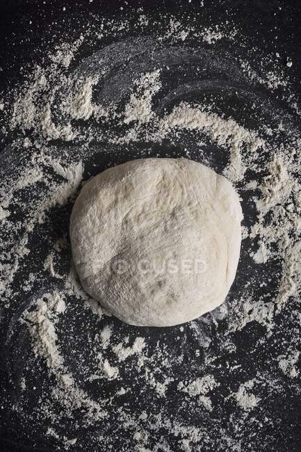 Pizza dough on a dark background with flour — Stock Photo