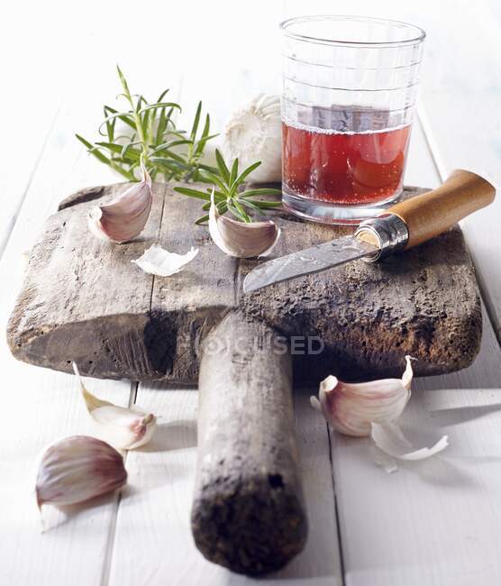 Cloves of garlic with red wine and a knife on an old wooden board — Stock Photo