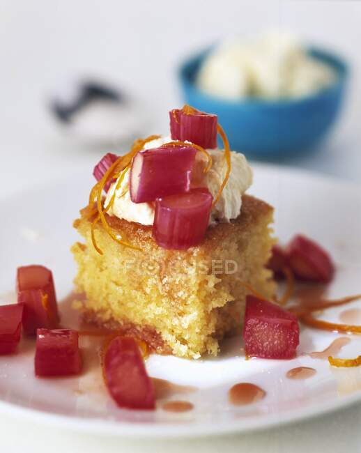 A slice of rhubarb and lemon cake with a bowl of cream in the background — Stock Photo