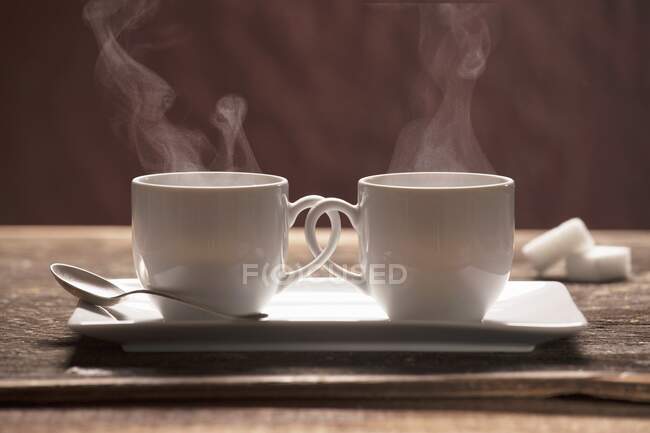Dos tazas de café humeantes con asas entrelazadas - foto de stock