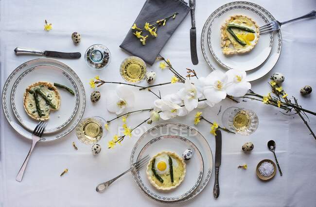 Spargelquiche mit gebratenem Wachtelei auf einem zu Ostern gedeckten Esstisch — Stockfoto