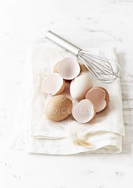 Huevos y cáscaras ecológicas con batidor en toalla de cocina - foto de stock