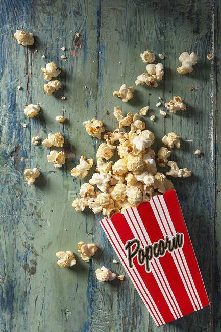 Boxed popcorn spilling out onto an aqua wooden board — Stock Photo