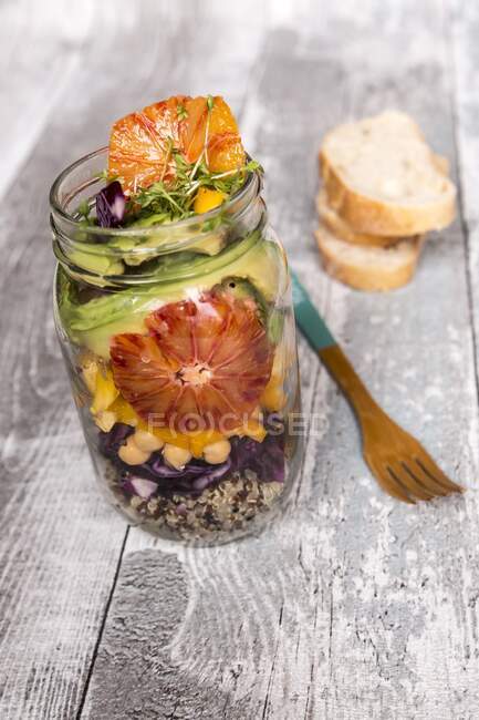 Салат из киноа в стеклянной банке с красной капустой, горохом, авокадо, апельсином и крессом — стоковое фото