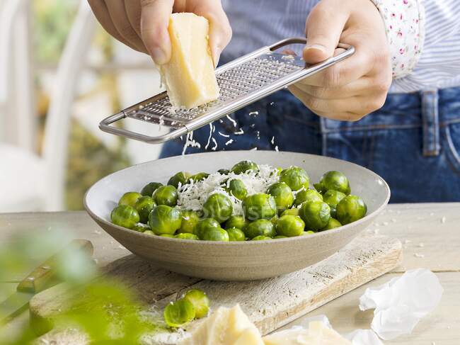 A man grating cheese over brussel's sprouts — Stock Photo