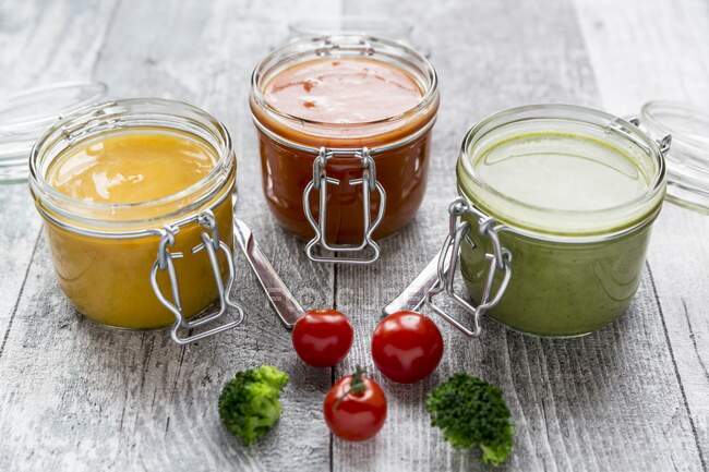 Varias sopas de colores en frascos de vidrio, sopa de brócoli, sopa de tomate, sopa de calabaza - foto de stock