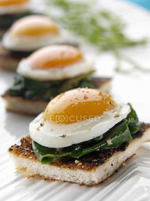 Peppered quails eggs in spinach on an English muffin canapes — Stock Photo